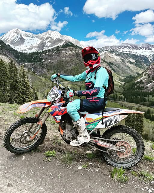 Dakota Freeman on his dirt bike on a mountain trail with snowy peaks behind him